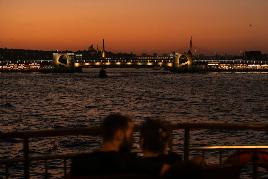 Couple enjoying sunset view of Istanbul's illuminated Galata Bridge.