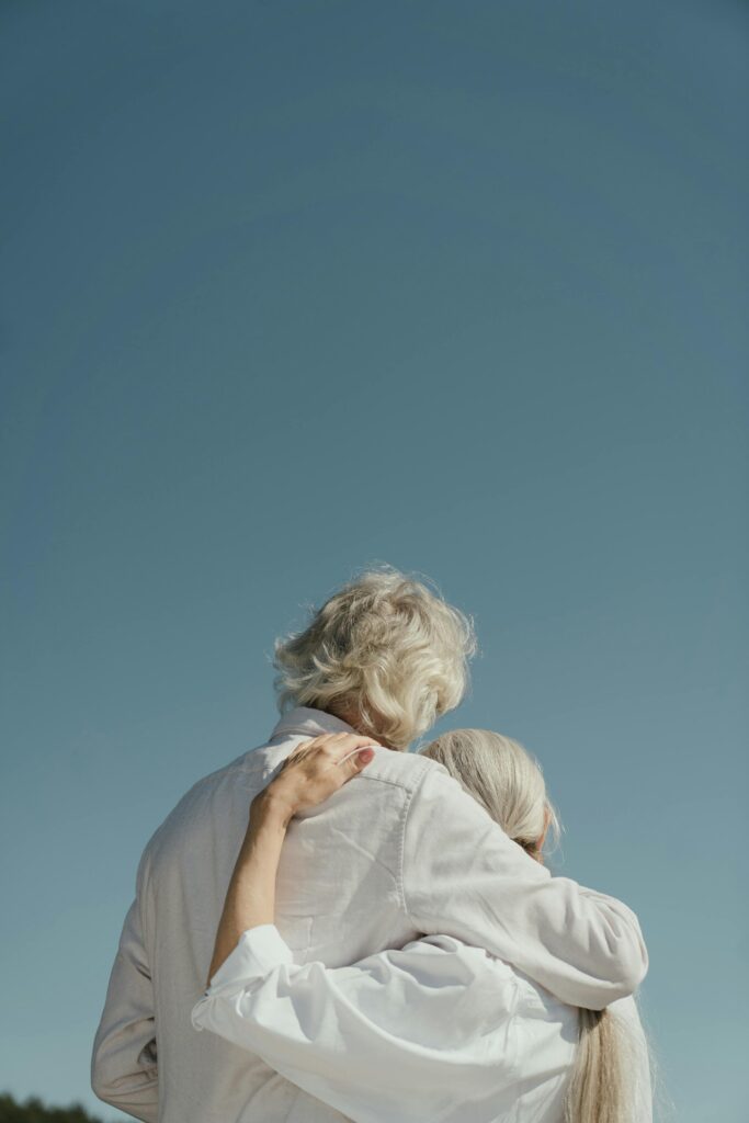 A senior couple hugs tenderly outdoors under a serene sky, symbolizing love and companionship.